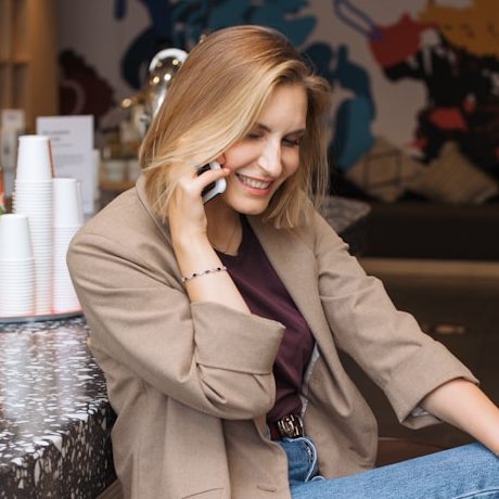 Telefonat vereinbaren Eine lächelnde Frau in einem Café, die mit einem Smartphone telefoniert.