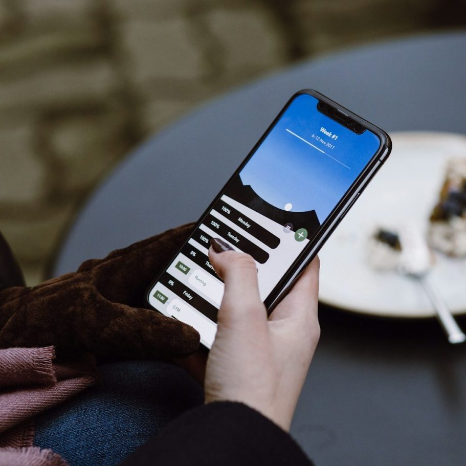 Termin buchen Person hält ein Smartphone mit einer App-Anzeige und einem blauem Himmel im Hintergrund.